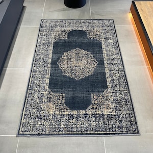 May include: A dark blue rug with a light beige pattern. The rug has a central design with a circular pattern inside a square frame.