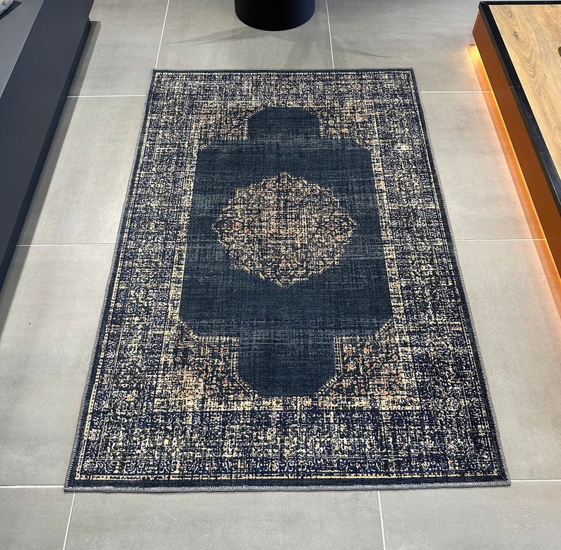 May include: A dark blue rug with a light beige pattern. The rug has a central design with a circular pattern inside a square frame.