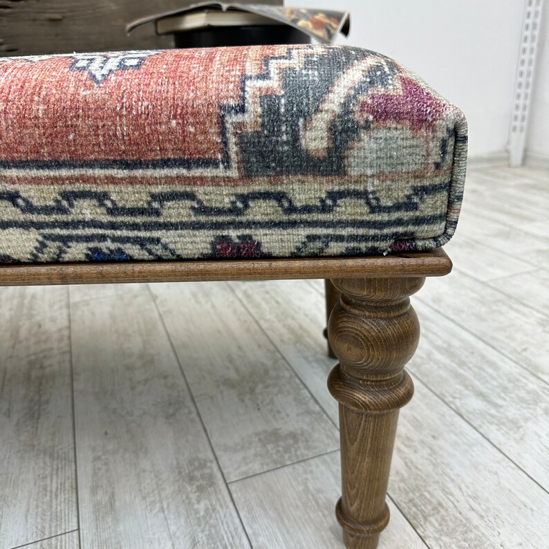May include: A wooden ottoman with turned legs and a patterned fabric top. The fabric is a traditional rug design with red, blue, and cream colors.