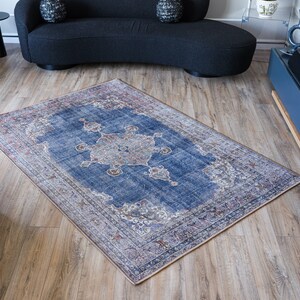 Op de afbeelding: Een blauw en cr&egrave;mekleurig tapijt met een vervaagde vintage look. Het tapijt heeft een centraal medaillonontwerp met ingewikkelde details. Het tapijt ligt op een houten vloer.