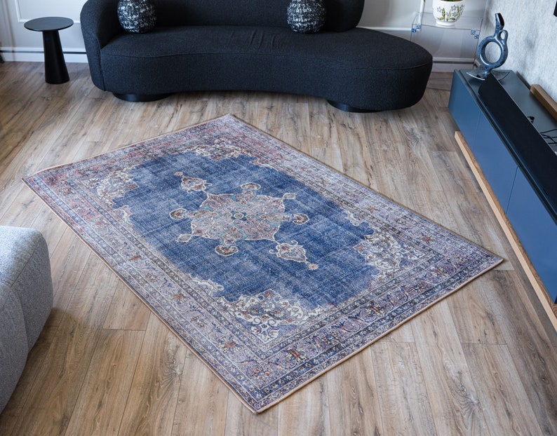 Op de afbeelding: Een blauw en cr&egrave;mekleurig tapijt met een vervaagde vintage look. Het tapijt heeft een centraal medaillonontwerp met ingewikkelde details. Het tapijt ligt op een houten vloer.