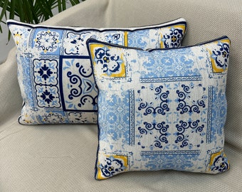 Puede incluir: Dos almohadas decorativas con un patrón geométrico azul y blanco. Las almohadas tienen un ribete amarillo y están sobre un sofá beige claro.