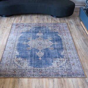 Op de afbeelding: Een blauw en cr&egrave;mekleurig tapijt met een bloemmotief in het midden. Het tapijt heeft een verweerde uitstraling en ligt op een houten vloer.