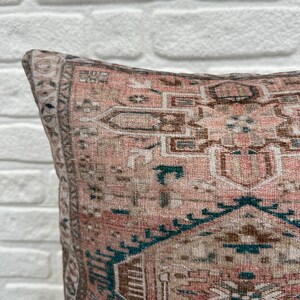 May include: A pink and brown patterned throw pillow with a teal border. The pillow has a traditional design with intricate details.