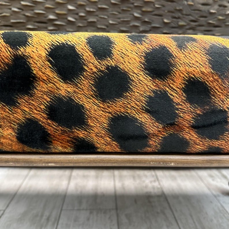 May include: Close-up of a rectangular object with a leopard print pattern. The pattern features black spots on a tan and brown background. The object is set on a light brown wooden frame.