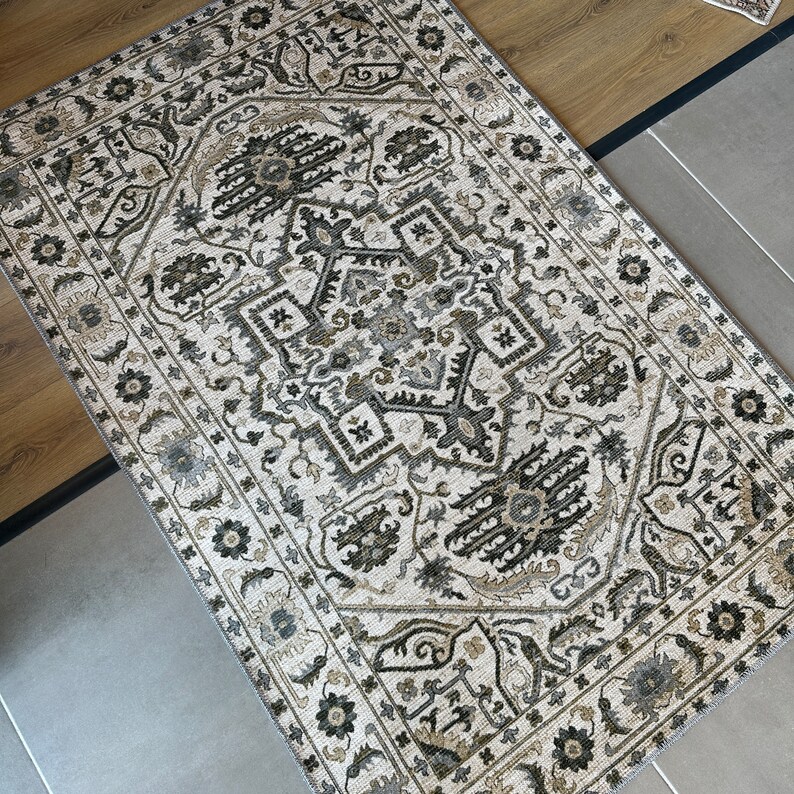 May include: A cream-colored rug with a black and brown geometric pattern. The rug has a traditional design with intricate details.