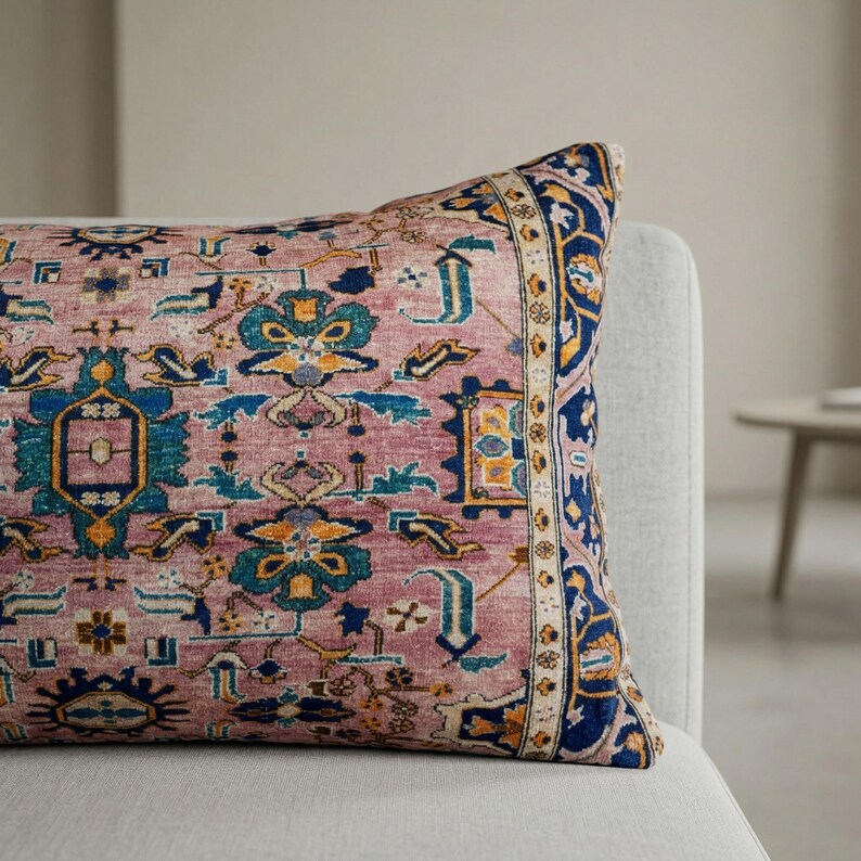 May include: A rectangular decorative pillow with a vintage rug design. The pillow features a dusty rose background with intricate patterns in blue, yellow, and teal. A navy blue border frames the design, adding a touch of elegance.