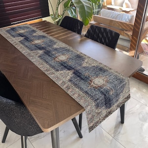 Peut inclure: Un chemin de table bleu et crème à motifs géométriques. Le chemin de table est posé sur une table en bois foncé avec deux chaises.