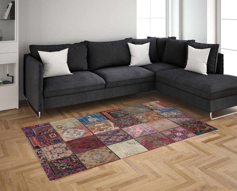 May include: A colorful patchwork rug with a variety of patterns and colors, including red, pink, blue, and green. The rug is made of different fabrics and textures, and it has a unique and eclectic style. The rug is placed in front of a gray sectional sofa with white pillows.
