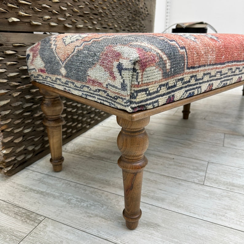May include: A wooden bench with turned legs and a colorful patterned fabric seat. The fabric has a traditional design with red, blue, and white colors.