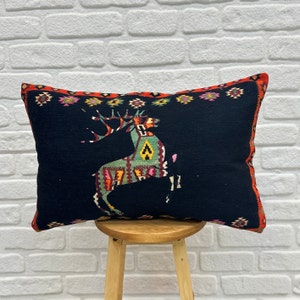 May include: Black cushion with a red, orange, green and yellow geometric deer design. The cushion is on a wooden stool.