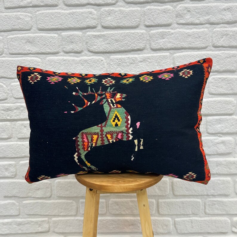 May include: Black cushion with a red, orange, green and yellow geometric deer design. The cushion is on a wooden stool.
