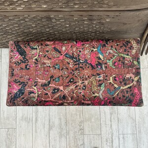 Peut inclure: Un ottoman rectangulaire de style vintage avec un motif floral color&eacute; dans des tons de rose, bleu et marron. L'ottoman est fait d'un tissu tiss&eacute; avec un aspect vieilli.