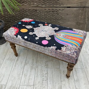 Pode incluir: Um otomano colorido e estampado com fundo preto e design de arco-íris. O otomano tem pernas de madeira e é feito de um tapete.