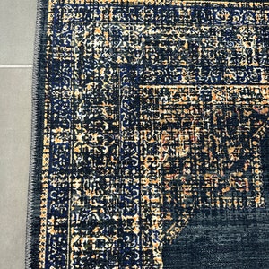 May include: A dark blue rug with a detailed pattern in shades of gold, black, and blue. The rug has a fringed edge.