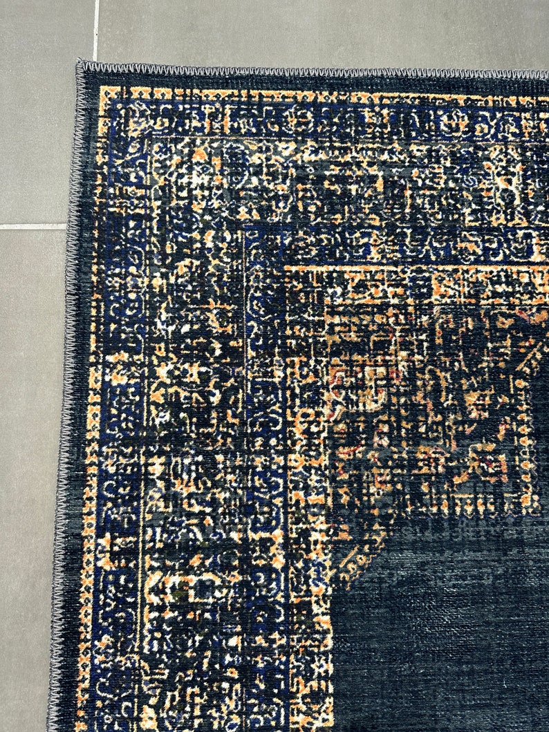 May include: A dark blue rug with a detailed pattern in shades of gold, black, and blue. The rug has a fringed edge.