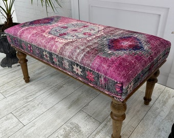 May include: A pink and black patterned bench with wooden legs. The bench is made from a traditional rug.