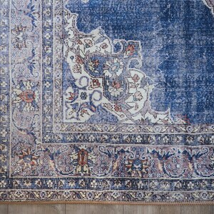 Op de afbeelding: Een blauw en cr&egrave;mekleurig tapijt met een gedetailleerde rand. Het tapijt heeft een verweerde, vintage uitstraling.
