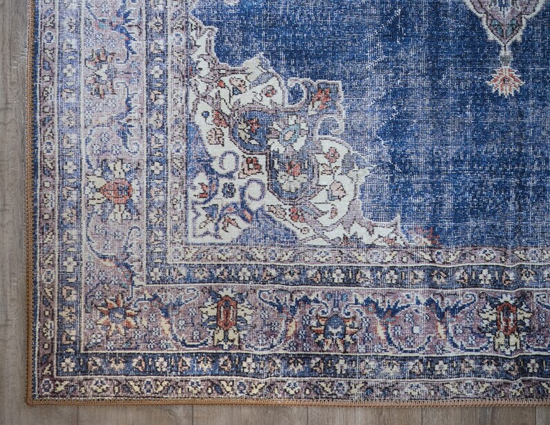 Op de afbeelding: Een blauw en cr&egrave;mekleurig tapijt met een gedetailleerde rand. Het tapijt heeft een verweerde, vintage uitstraling.