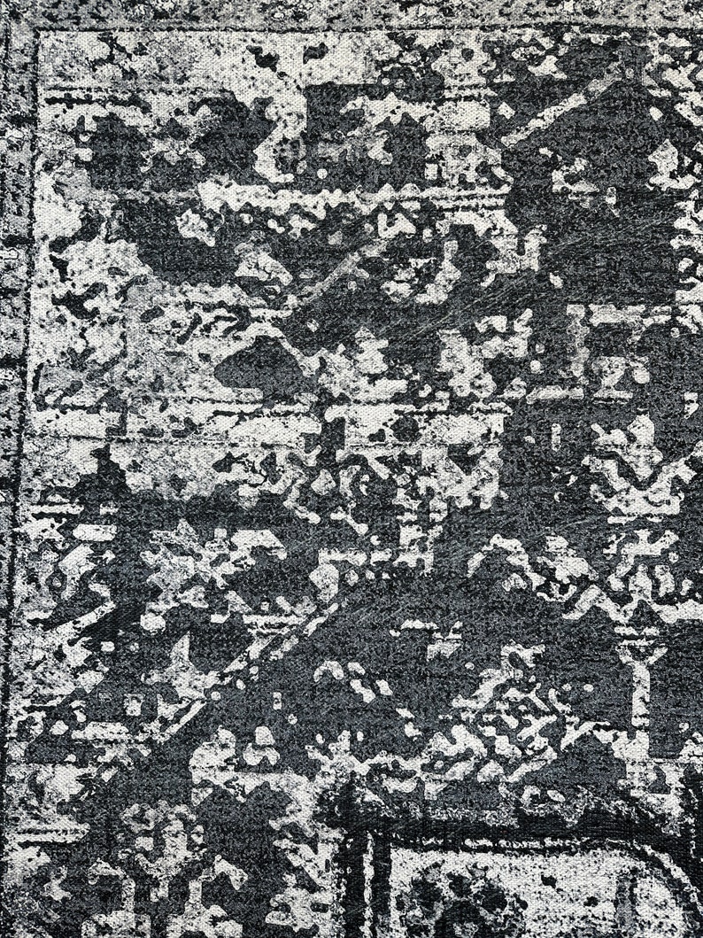 May include: A black and white area rug with a distressed, vintage look. The rug has a geometric pattern with a faded, worn appearance.