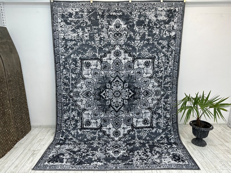 May include: A black and white area rug with a large, intricate, floral pattern in the center. The rug has a distressed, vintage look.