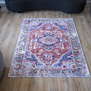 K&ouml;nnte beinhalten: Ein rot-blau-wei&szlig;er Teppich mit traditionellem persischem Design. Der Teppich hat einen wei&szlig;en Hintergrund mit einem zentralen Medaillon und komplizierten Blumenmustern.