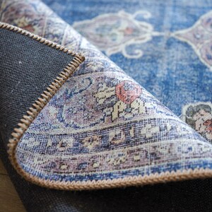 Op de afbeelding: Close-up van een blauw en wit gepatroneerd tapijt met een bruine franje. Het tapijt is omgeslagen om de achterkant te laten zien.