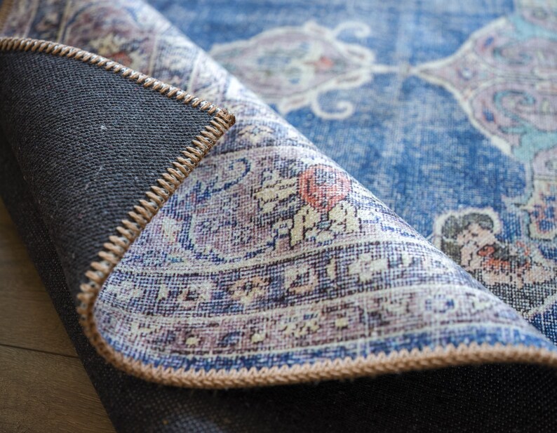 Op de afbeelding: Close-up van een blauw en wit gepatroneerd tapijt met een bruine franje. Het tapijt is omgeslagen om de achterkant te laten zien.