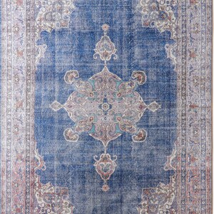 Op de afbeelding: Een vintage-stijl tapijt met een blauwe achtergrond en ingewikkelde bloemmotieven in tinten roze, wit en beige. Het tapijt heeft een vervaagde, verweerde uitstraling, waardoor het een unieke en antieke uitstraling heeft.