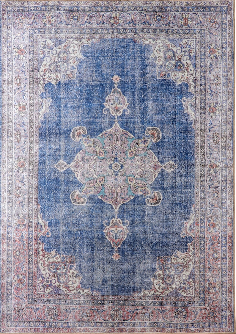 Op de afbeelding: Een vintage-stijl tapijt met een blauwe achtergrond en ingewikkelde bloemmotieven in tinten roze, wit en beige. Het tapijt heeft een vervaagde, verweerde uitstraling, waardoor het een unieke en antieke uitstraling heeft.