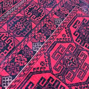 May include: Close-up of a red and black patterned rug. The rug features geometric designs in black against a red background. The pattern includes repeating shapes and lines, creating a detailed and textured appearance. The rug's color palette is dominated by deep reds and blacks.