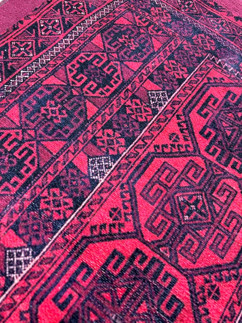 May include: Close-up of a red and black patterned rug. The rug features geometric designs in black against a red background. The pattern includes repeating shapes and lines, creating a detailed and textured appearance. The rug's color palette is dominated by deep reds and blacks.