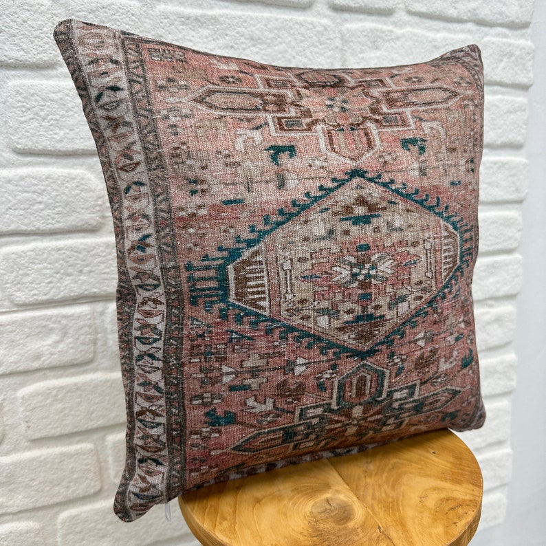 May include: A decorative throw pillow with a pink, brown, and teal geometric pattern. The pillow is made of a soft, woven fabric and has a subtle distressed look.