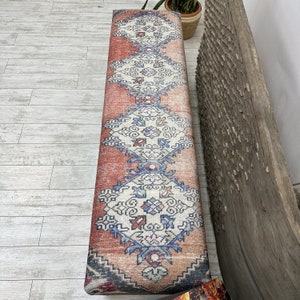 May include: A bench with a colorful patterned cushion. The cushion has a red, white, and blue design with intricate patterns. The bench is made of wood and has a natural finish.