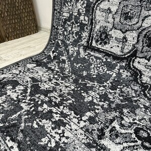 May include: A black and white area rug with a distressed, vintage-inspired pattern. The rug has a subtle geometric design with faded and worn details.