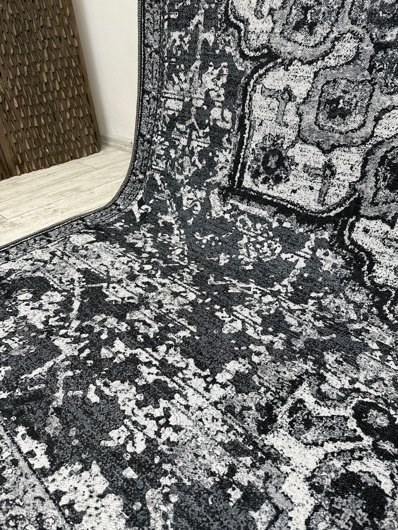 May include: A black and white area rug with a distressed, vintage-inspired pattern. The rug has a subtle geometric design with faded and worn details.