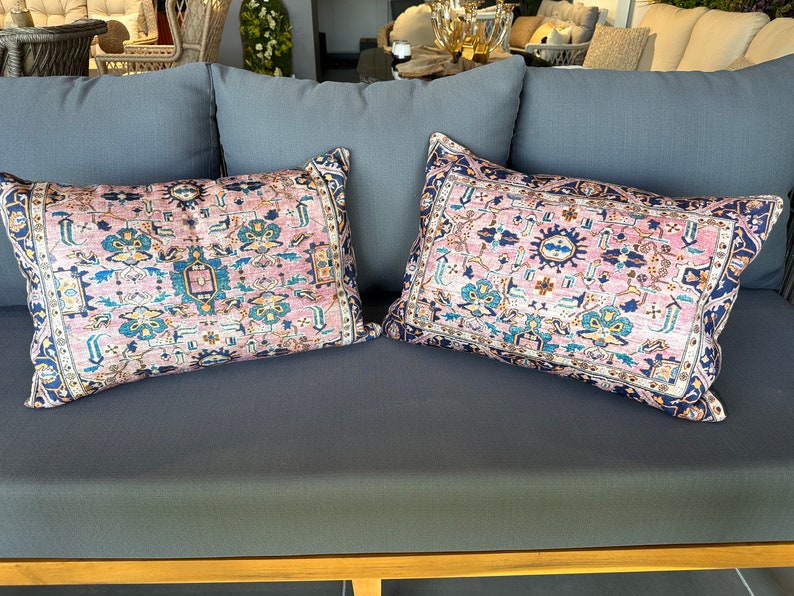 May include: Two rectangular throw pillows with a vintage rug design. The pillows feature a pink background with a detailed pattern in shades of blue, teal, and yellow. The borders are dark blue.