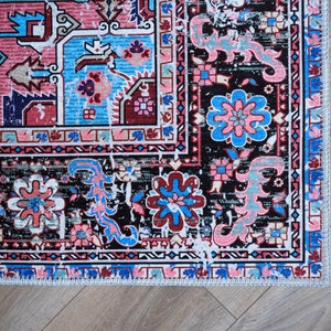 K&ouml;nnte beinhalten: Ein bunter Teppich mit schwarzem Hintergrund und komplizierten floralen Mustern in Rosa-, Blau- und Wei&szlig;t&ouml;nen. Der Teppich hat einen Fransenrand.