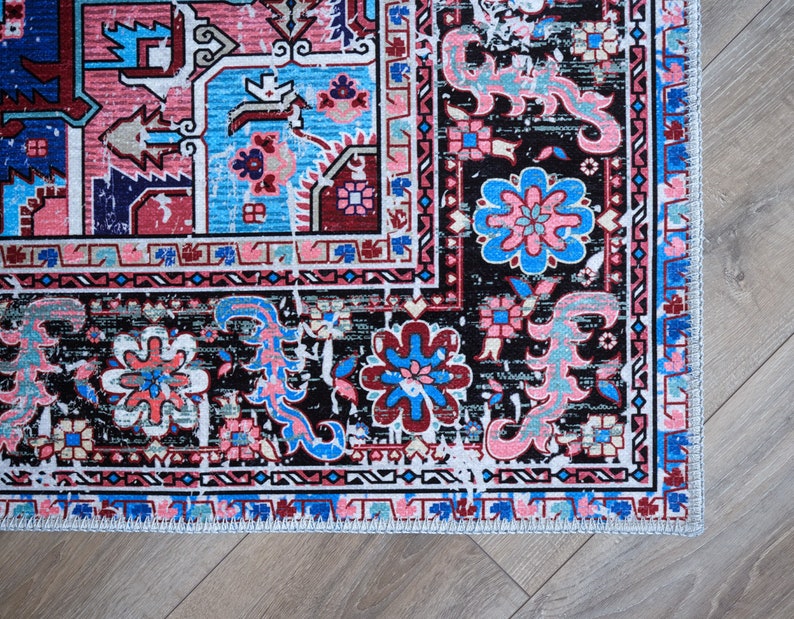K&ouml;nnte beinhalten: Ein bunter Teppich mit schwarzem Hintergrund und komplizierten floralen Mustern in Rosa-, Blau- und Wei&szlig;t&ouml;nen. Der Teppich hat einen Fransenrand.
