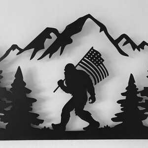 Puede incluir: Arte de pared de metal negro con una silueta de Bigfoot caminando por una cordillera con una bandera estadounidense en la mano.