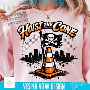 Peut inclure: Sweat-shirt rose clair avec l'inscription "Hoist the Cone" en orange et noir. Le motif comprend un c&ocirc;ne de signalisation, un drapeau t&ecirc;te de mort et une silhouette de ville. Illustration graphique.