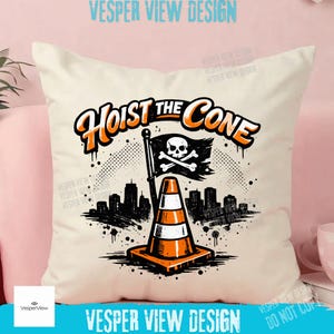 Peut inclure: Coussin cr&egrave;me avec un motif graphique repr&eacute;sentant un c&ocirc;ne de signalisation, un drapeau t&ecirc;te de mort et une ligne d'horizon urbaine. Le texte "Hoist the Cone" est en orange et noir. Le coussin est sur une surface rose.