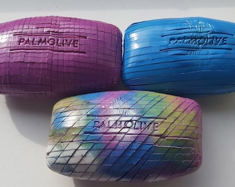 May include: Three bars of soap with the word "PALMOLIVE" embossed on them. The bars are purple, blue, and a multi-coloured swirl pattern.