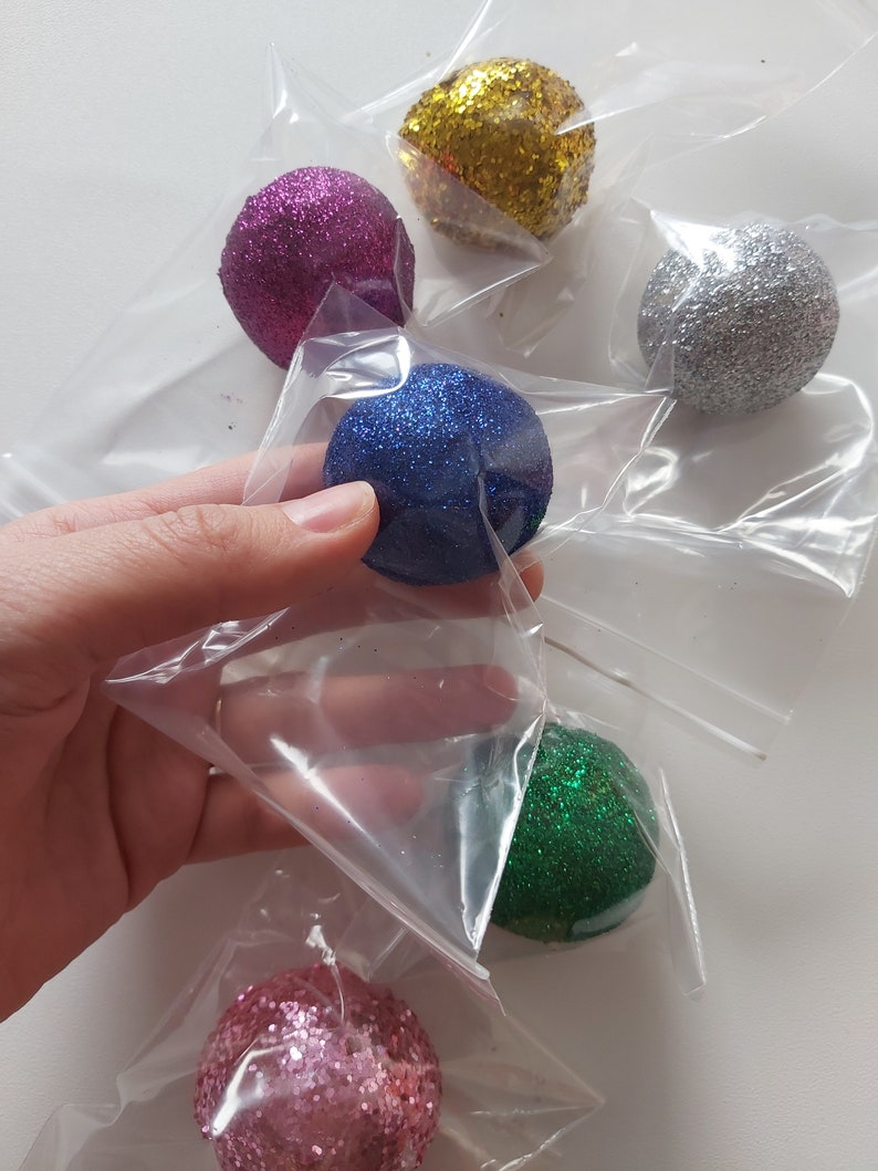 May include: Six small, round, glitter-covered ornaments in individual plastic bags. The ornaments are pink, blue, green, gold, silver, and a lighter shade of pink.