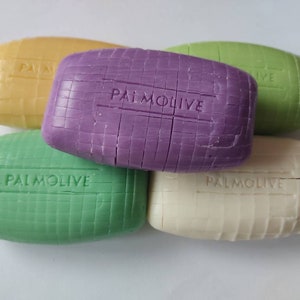 May include: Five bars of Palmolive soap, in various colours, including yellow, purple, green, and white. Each bar has the word "Palmolive" embossed on it.