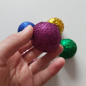 May include: A collection of five small, glittery Christmas ornaments in various colors, including purple, blue, green, and gold.