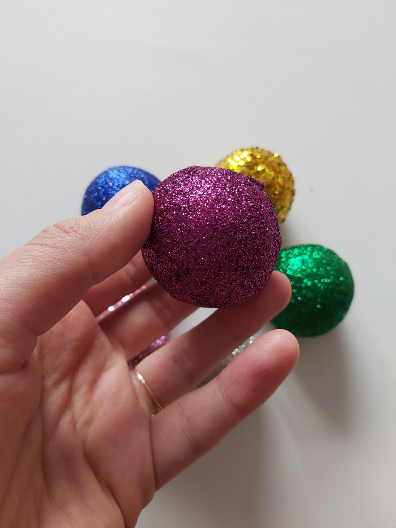 May include: A collection of five small, glittery Christmas ornaments in various colors, including purple, blue, green, and gold.
