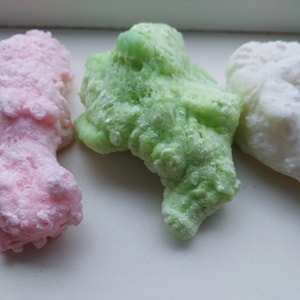Pode incluir: Três itens decorativos feitos de um material espumoso. Os itens têm a forma de figuras abstratas e são de cor rosa, verde e branco.