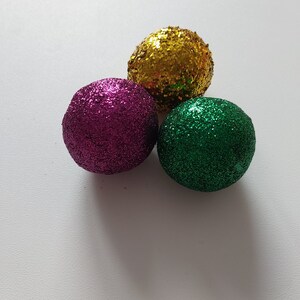 May include: Three round ornaments with glitter. The ornaments are gold, purple, and green.