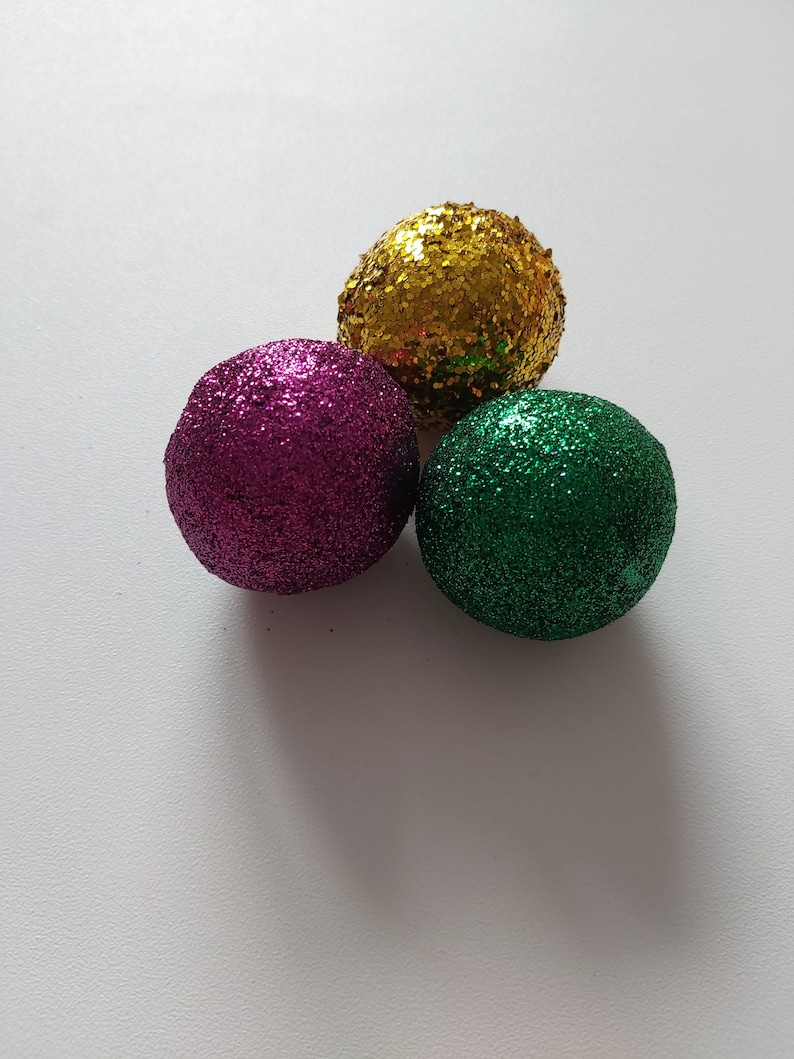 May include: Three round ornaments with glitter. The ornaments are gold, purple, and green.